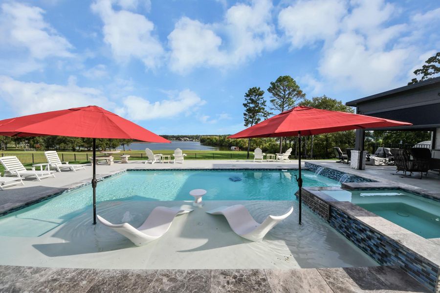 Luxurious outdoor oasis featuring a sparkling pool with stylish lounge chairs, vibrant red umbrellas, and a stunning lake view. Perfect for relaxation and entertaining.