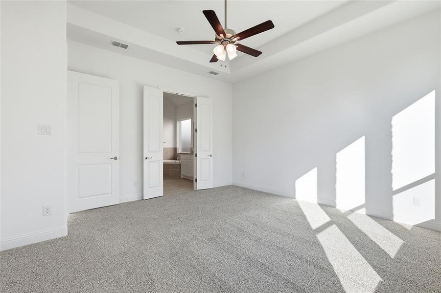 Unfurnished bedroom featuring a raised ceiling, ceiling fan, connected bathroom, and light colored carpet Unfurnished bedroom featuring a raised ceiling, ceiling fan, connected bathroom, and light colored carpet