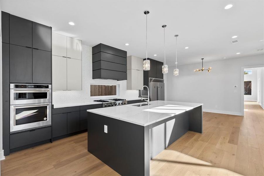 Kitchen with custom exhaust hood, hanging light fixtures, a large island with sink, and light hardwood / wood-style flooring