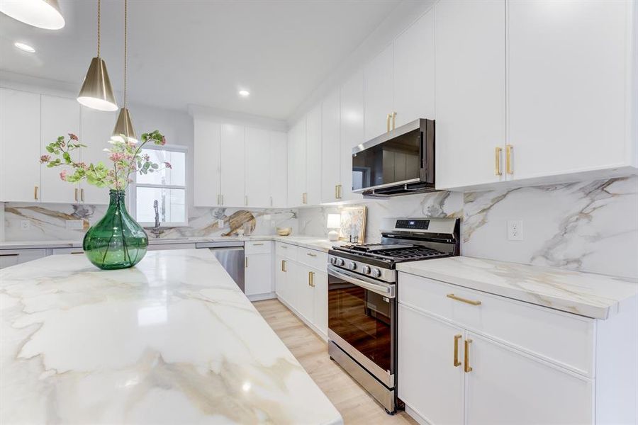 This stunning kitchen features gold hardware, quartz countertops, gas range, and stainless steel appliances. There is plenty of storage space in the cabinets.