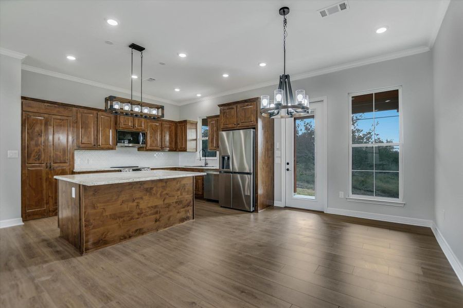 Kitchen with a chandelier, hanging light fixtures, a kitchen island, ornamental molding, and appliances with stainless steel finishes