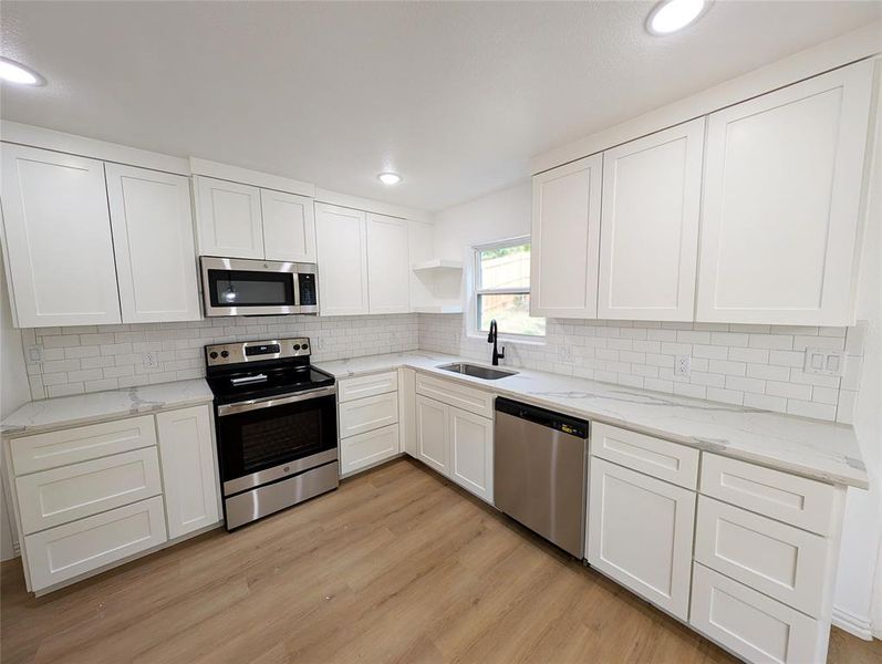 Kitchen with white cabinetry, stainless steel appliances, light wood-type flooring, light stone counters, and sink