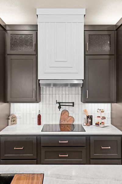 Bar area with ventilation hood, black electric cooktop, and backsplash Bar area with ventilation hood, black electric cooktop, and backsplash