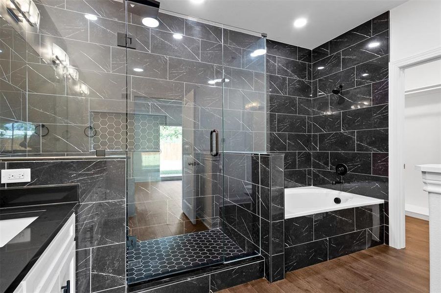Bathroom featuring wood finished floors, a garden tub, a marble finish shower, and double vanity