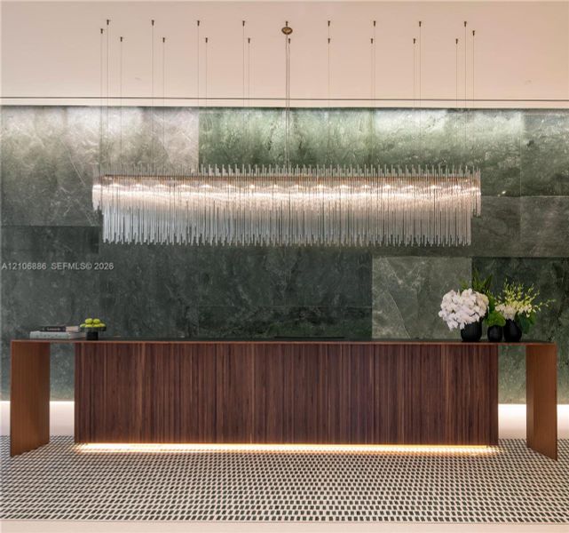 Large-scale linear chandelier with crystalline fringe, wood-veneer floating desk with base accent lighting, and full-height green-toned stone feature wall