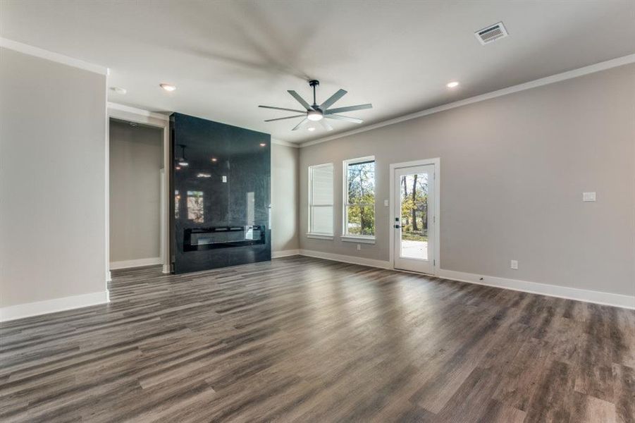 Unfurnished living room with dark wood-type flooring, crown molding, ceiling fan, recessed lighting, and a fireplace
