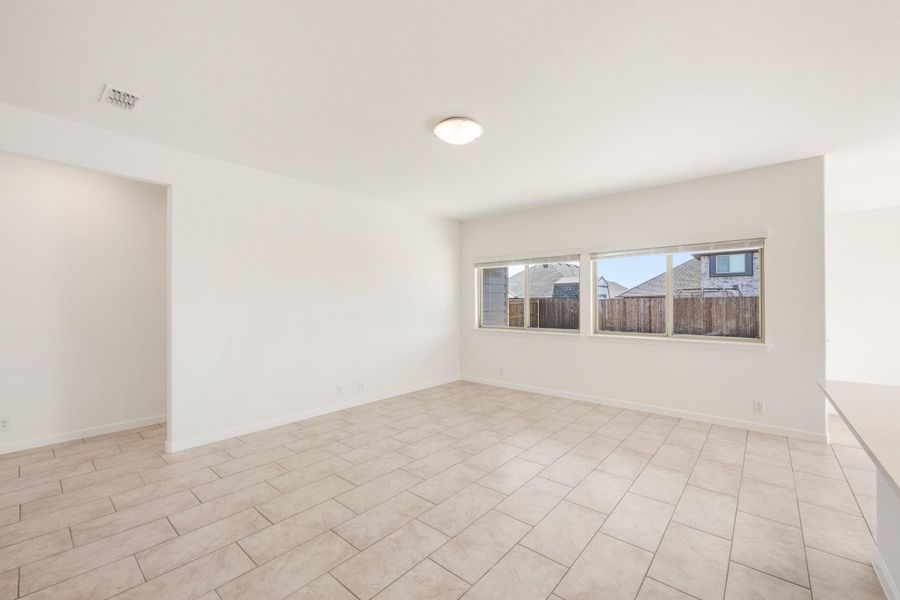 Empty living room with light tile floors, white walls, and a window overlooking a backyard fence