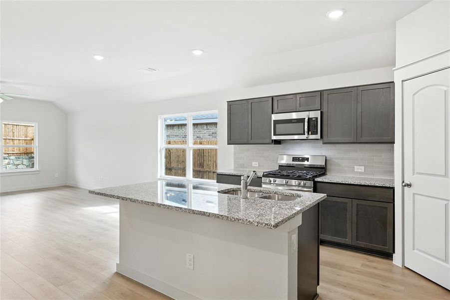 Kitchen featuring appliances with stainless steel finishes, light stone countertops, tasteful backsplash, plenty of natural light, and vaulted ceiling