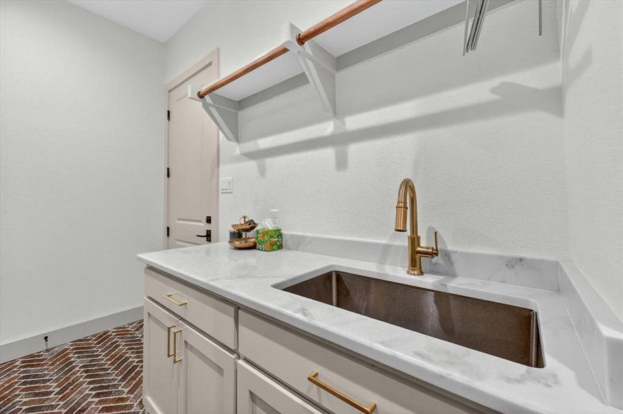 Herringbone brick-patterned flooring complements a light-toned cabinetry vanity with gold-finish hardware
