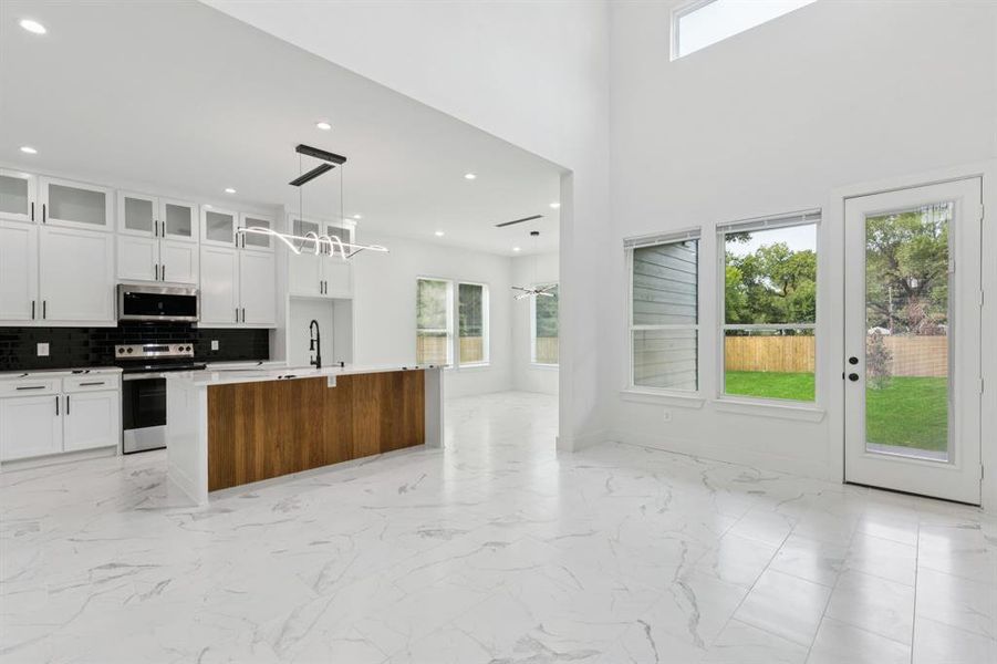 Kitchen featuring plenty of natural light, glass insert cabinets, light marble finish floors, a high ceiling, and recessed lighting Kitchen featuring plenty of natural light, glass insert cabinets, light marble finish floors, a high ceiling, and recessed lighting