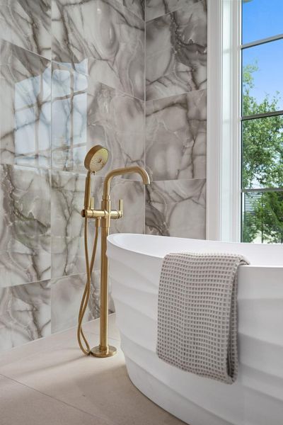 Indulge in a luxurious freestanding tub, highlighted by a brass floor-mounted faucet against a striking marble-tiled wall.
