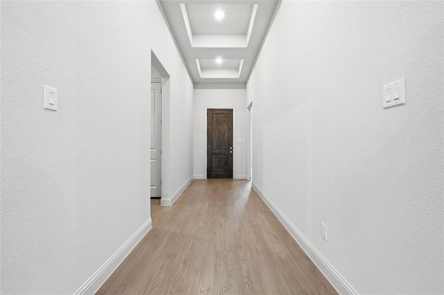 Hall featuring light wood-type flooring, a raised ceiling, and a textured wall