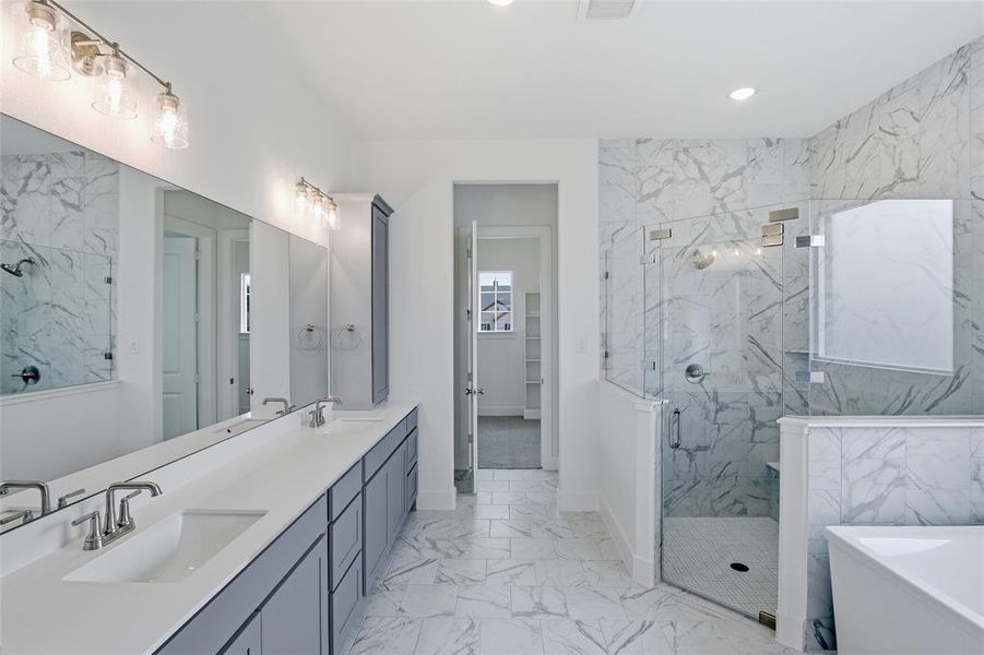 Bathroom featuring light marble finish floors, double vanity, a marble finish shower, a freestanding tub, and a walk in closet