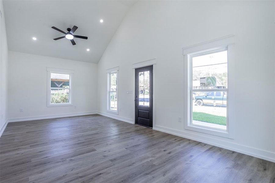 Spacious interior featuring a vaulted ceiling with a ceiling fan, recessed lighting, wood-finish flooring, white baseboards, and white window trim