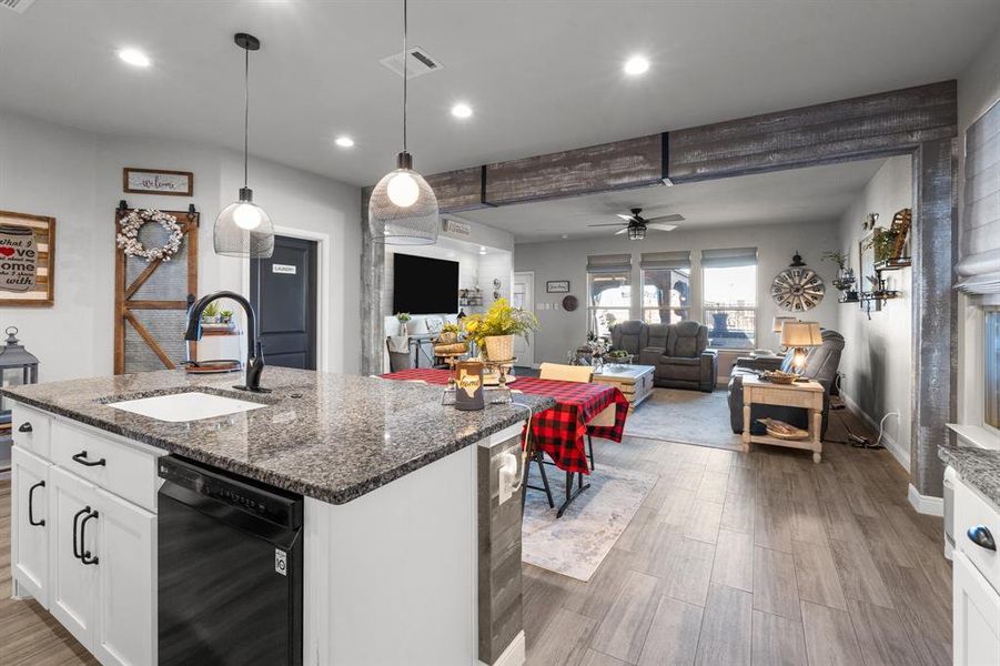 Kitchen with a kitchen island with sink, sink, dark stone countertops, white cabinets, and black dishwasher