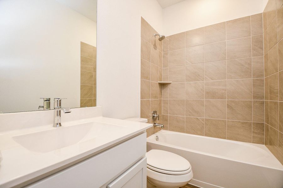 This bathroom features a modern, sleek design with neutral-toned tile walls surrounding a bathtub and shower. It includes a clean, white vanity with a stylish faucet, providing a fresh and inviting look.