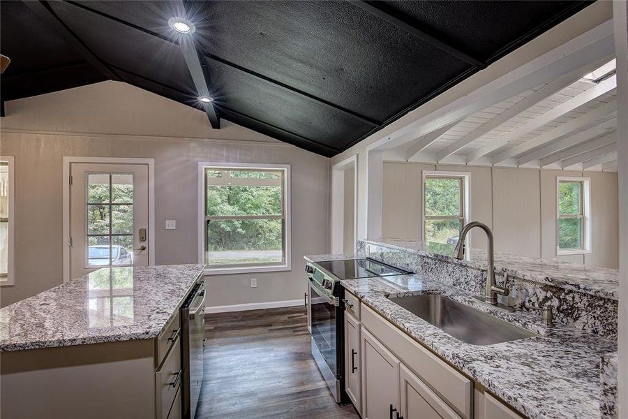 Kitchen with an island with sink, sink, white cabinets, and electric stove