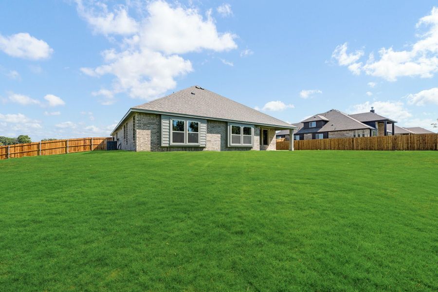 Rear view of single-story brick home with large fenced backyard and green lawn