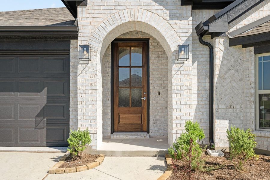 Wood front door with glass panels set in brick archway, with wall sconces and attached garage