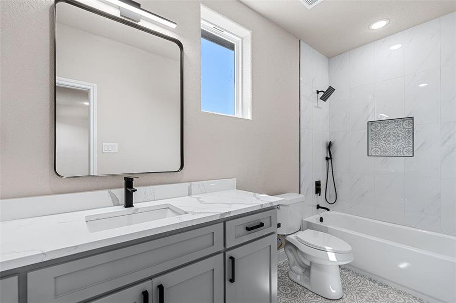 Full bathroom featuring tile patterned flooring, vanity, tiled shower / bath combo, and toilet