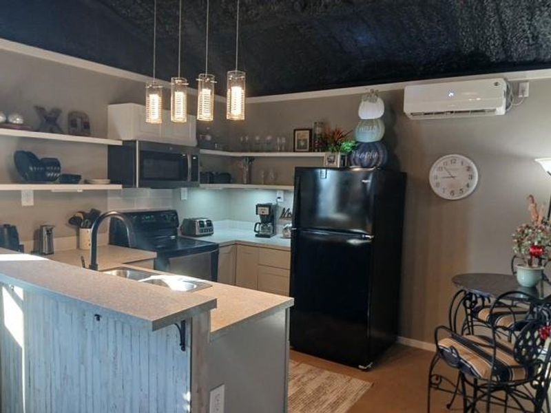 Kitchen featuring light countertops, black appliances, open shelves, decorative light fixtures.