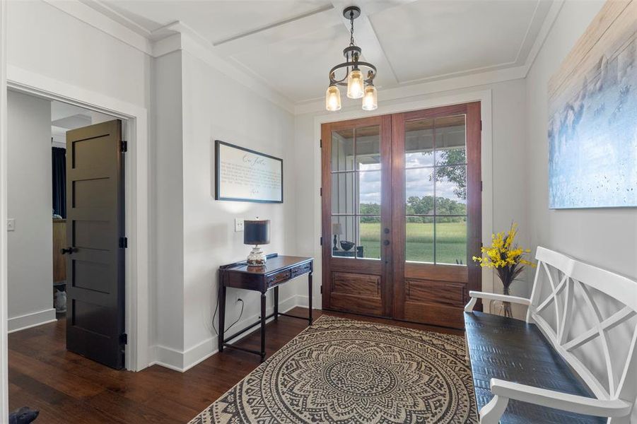 Welcoming entryway featuring rich wood flooring, glass-paneled front doors, elevated ceiling detail, and peaceful acreage views that set the tone for the home’s refined country charm.
