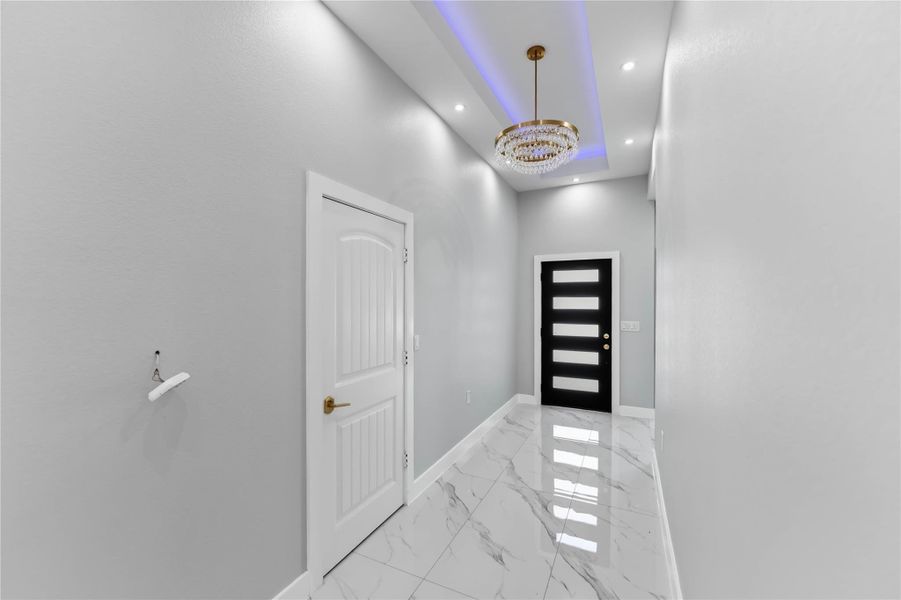 Step into elegance through this sleek, modern front door, complemented by a luxurious chandelier and pristine marble flooring.