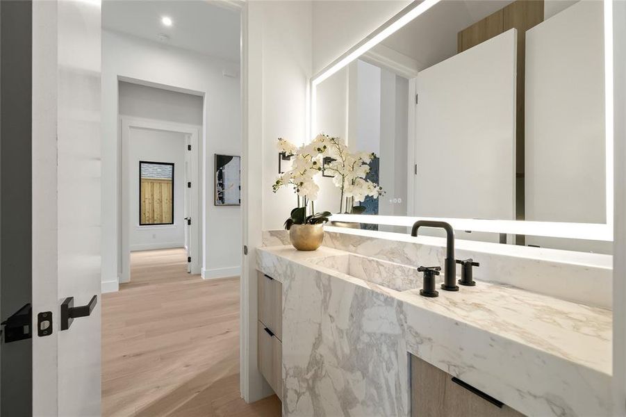 Integrated marble vanity with an undermount sink, matte black three-piece faucet, and a large illuminated mirror Integrated marble vanity with an undermount sink, matte black three-piece faucet, and a large illuminated mirror