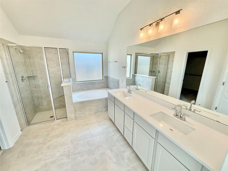 Full bath featuring a bath, a shower stall, double vanity, lofted ceiling, and light tile patterned floors