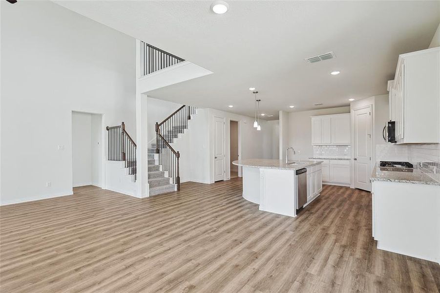 Kitchen with sink, light hardwood / wood-style floors, decorative backsplash, an island with sink, and white cabinetry