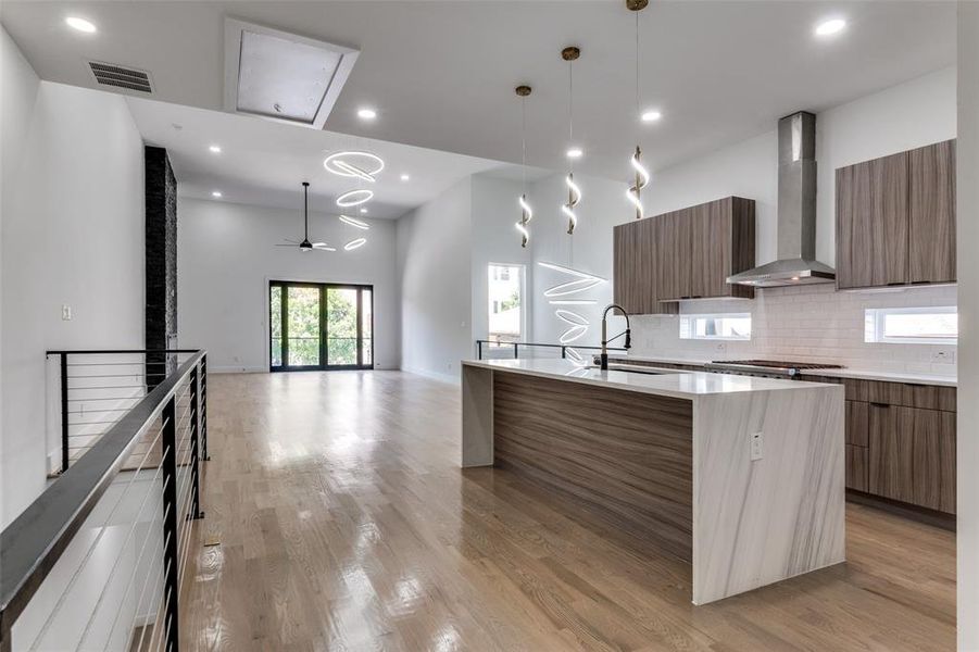 Kitchen featuring modern cabinets, wall chimney exhaust hood, an island with sink, light wood-type flooring, and light countertops