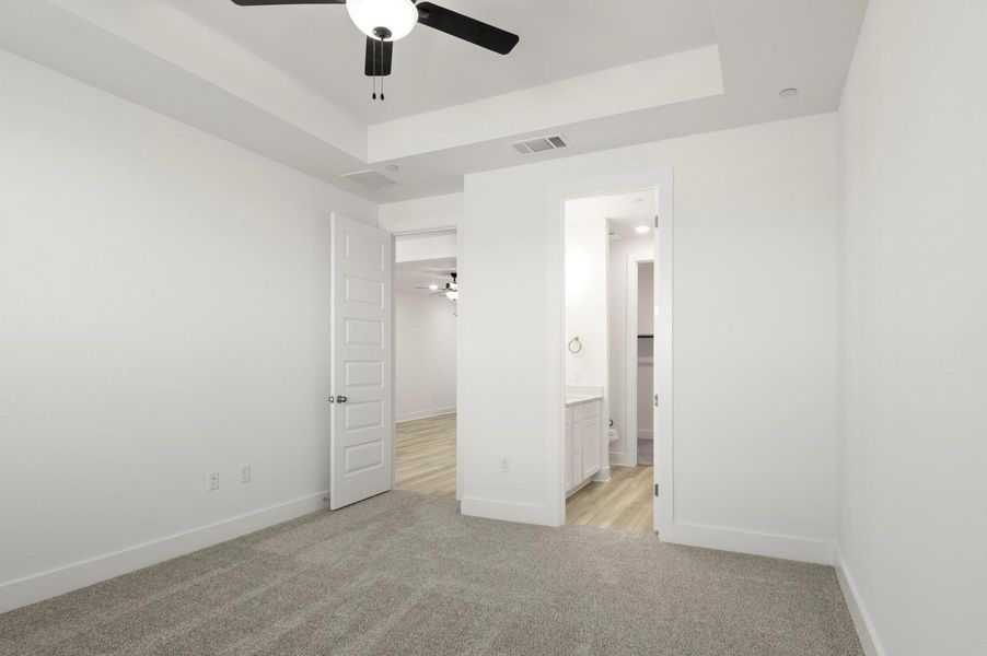 Unfurnished bedroom featuring light colored carpet, a ceiling fan, a tray ceiling, and ensuite bathroom