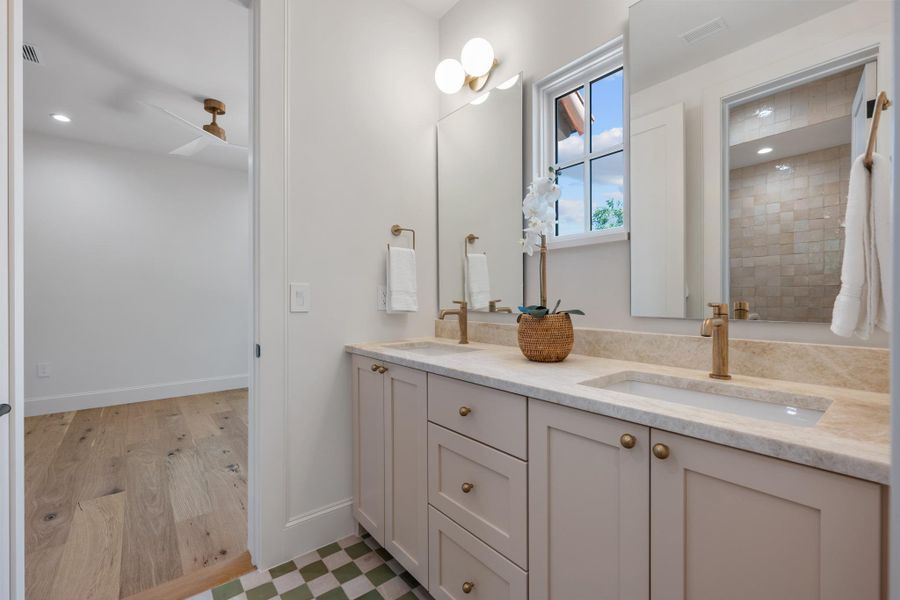 Double vanities with stone countertops stand beneath dual mirrors in this modern bathroom.