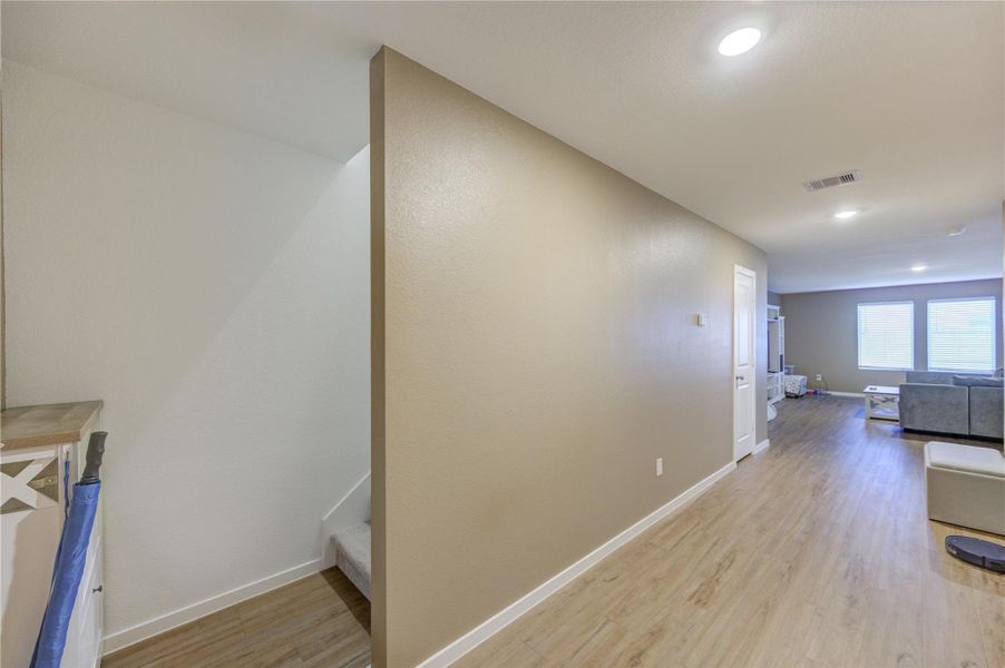 This photo shows a modern, open-concept living area with vinyl plank flooring, neutral walls, and recessed lighting. A staircase is visible, leading to another level, and large windows provide natural light to the spacious room.