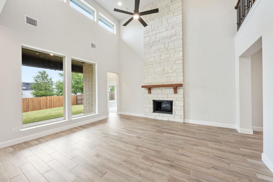 Open living room with two-story ceiling, stone fireplace, ceiling fan, and wood-look tile floors