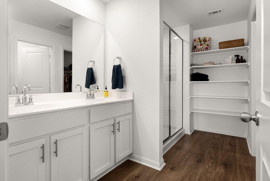 Full bathroom with a spacious closet, double vanity, a stall shower, and dark wood-style flooring