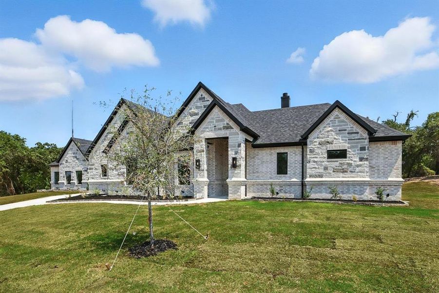 French country style house with stone siding, a chimney, a front lawn, and brick siding