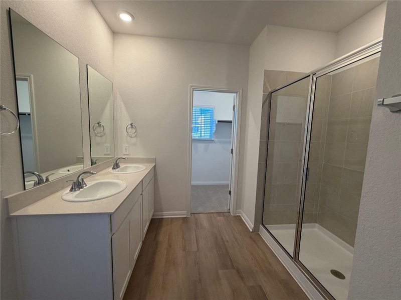 Full bath featuring double vanity, dark wood-style floors, a stall shower, and a spacious closet