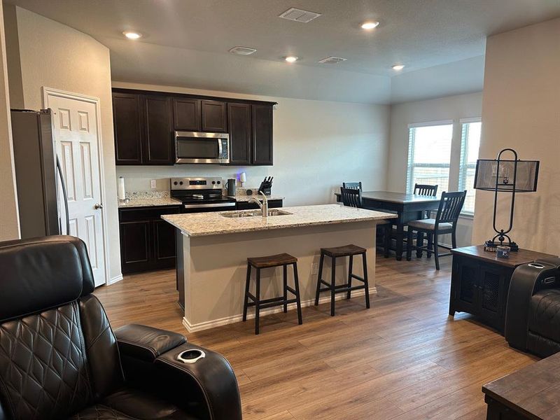 Kitchen with appliances with stainless steel finishes, light wood finished floors, light stone counters, a breakfast bar area, and an island with sink