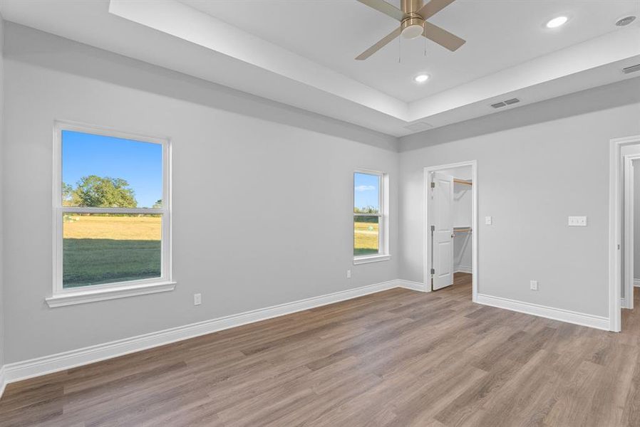 Unfurnished bedroom with a tray ceiling, a walk in closet, ceiling fan, wood finished floors, and recessed lighting