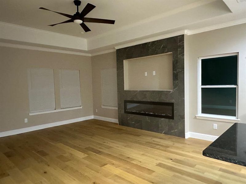 Unfurnished living room featuring ceiling fan, hardwood / wood-style flooring, a tray ceiling, a large fireplace, and crown molding