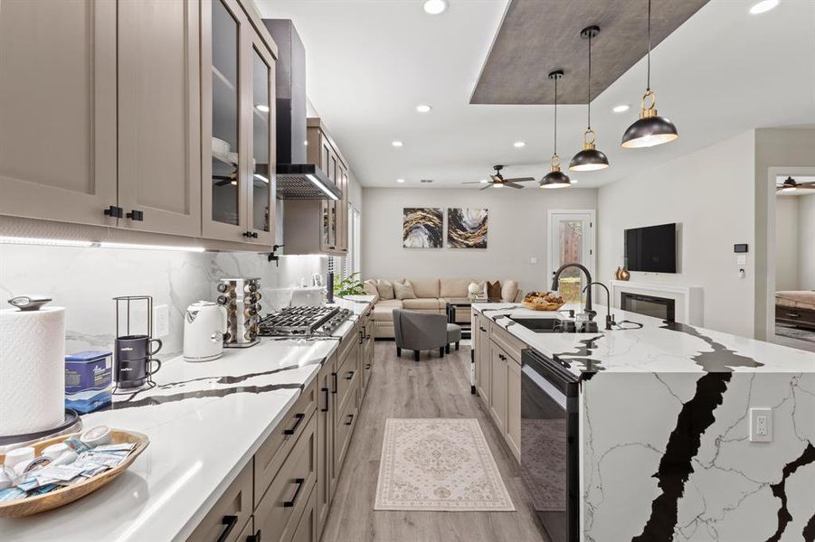 Kitchen with light stone countertops, open floor plan, glass insert cabinets, hanging light fixtures, and ceiling fan
