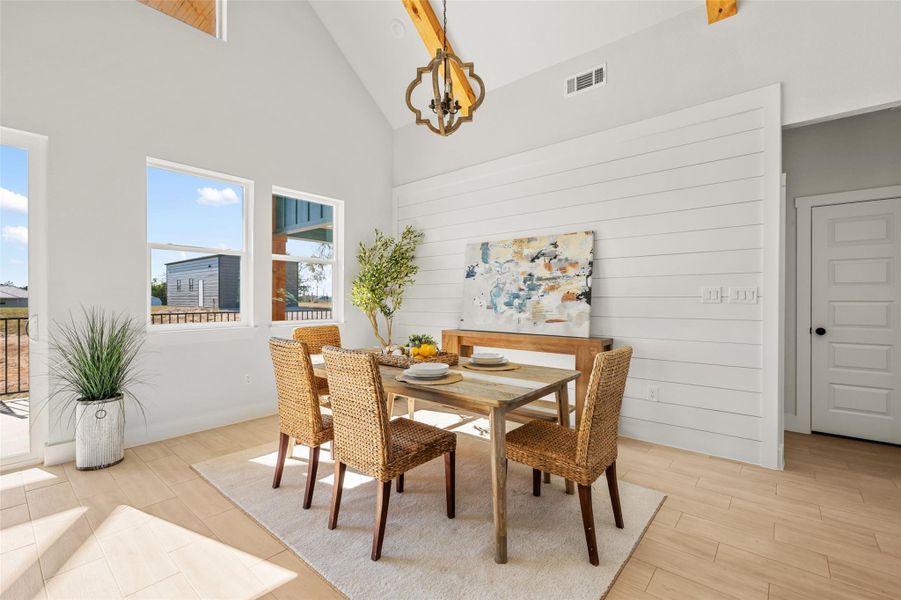 Dining space with high vaulted ceiling, wood tiled floors, wood walls, and a chandelier