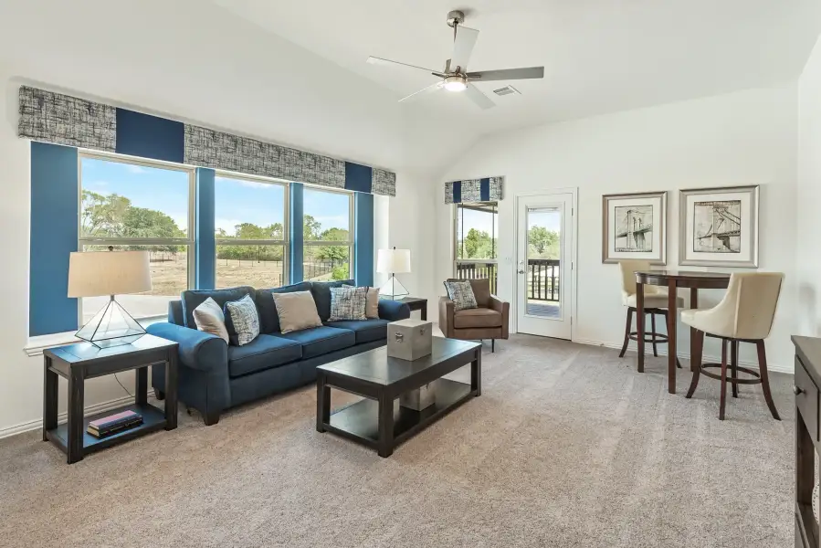 Living room with blue sofa, vaulted ceiling, ceiling fan, and large windows with outdoor views