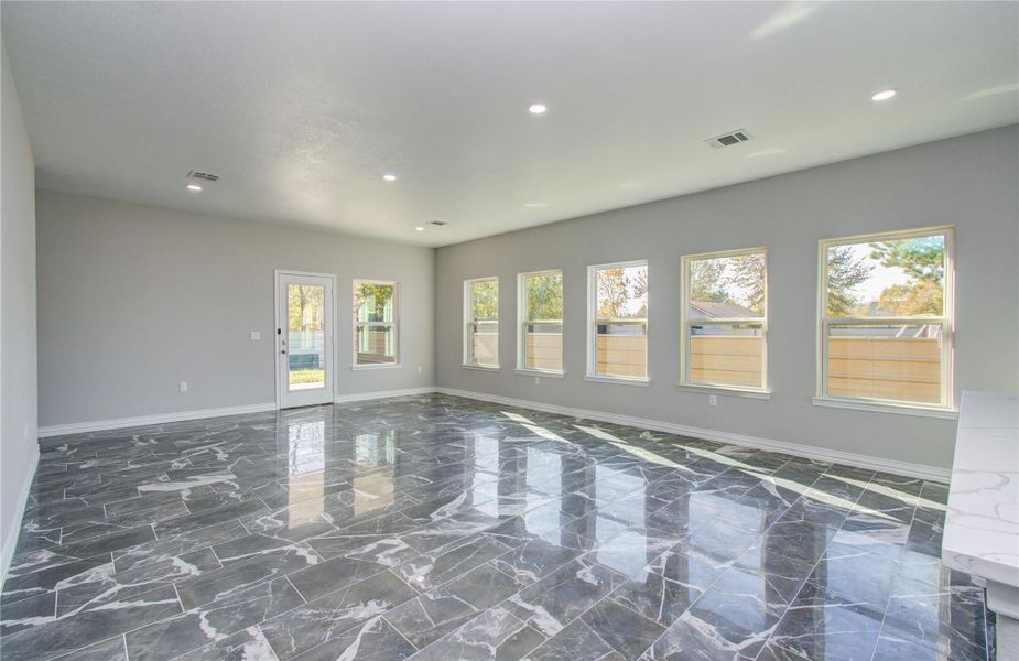 This spacious room features sleek, dark marble flooring and abundant natural light from multiple large windows. The neutral walls and recessed lighting create a modern, open atmosphere, with a door leading to an outdoor area.
