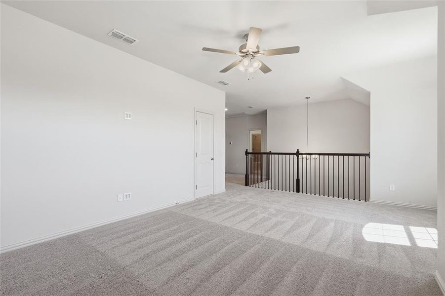 Carpeted interior space featuring a ceiling fan, vaulted ceiling, white walls, and black metal railing