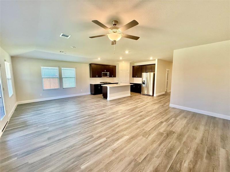 Expansive open-concept living area featuring wood-finish flooring, a kitchen island, recessed lighting, and a ceiling fan Expansive open-concept living area featuring wood-finish flooring, a kitchen island, recessed lighting, and a ceiling fan