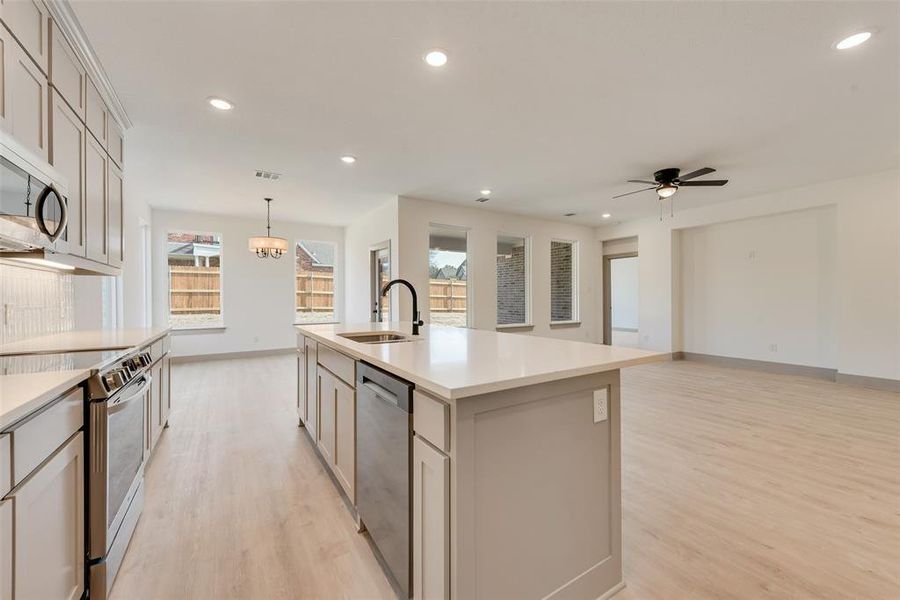 Kitchen with sink, appliances with stainless steel finishes, hanging light fixtures, an island with sink, and light wood-type flooring