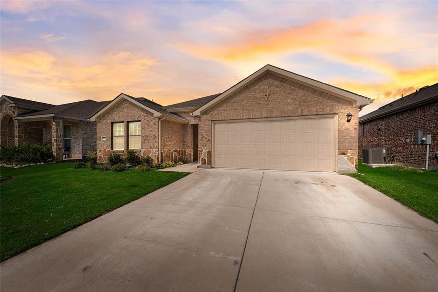 Single story home featuring brick siding, a front lawn, driveway, an attached garage, and stone siding Single story home featuring brick siding, a front lawn, driveway, an attached garage, and stone siding