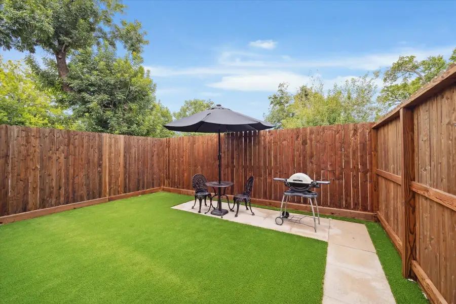 A cozy, private backyard with a wooden fence, grass, and a small patio area.You can enjoy a fresh morning coffee under the umbrella and chairs, perfect for outdoor dining, along with a grill for barbecuing.